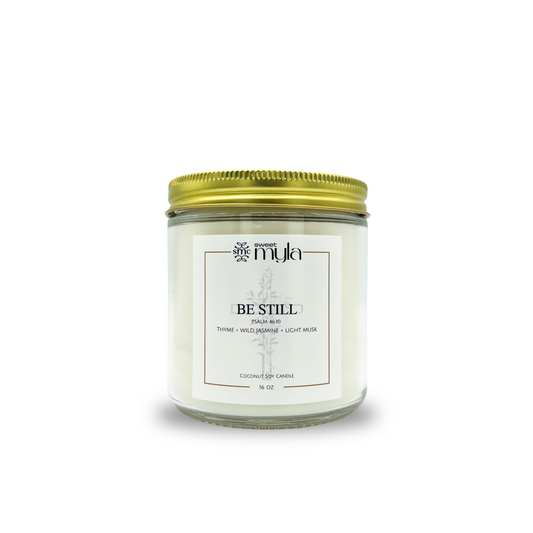 Candle jar with a gold lid labeled 'Be Still' on a white background