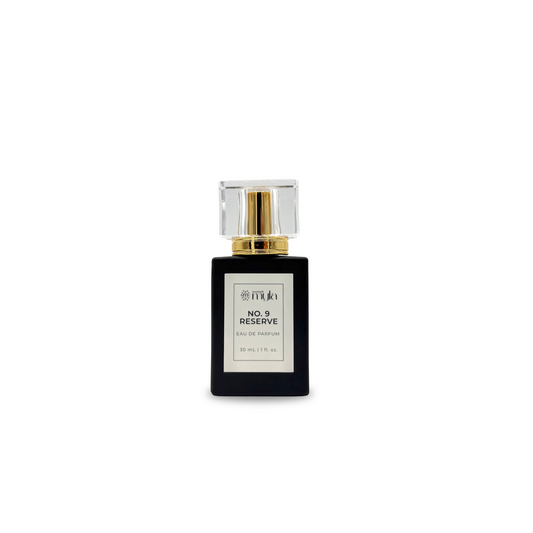 A rectangular black perfume bottle with a clear faceted cap and a gold collar, featuring a white label that reads 'NO. 9 RESERVE EAU DE PARFUM' by Sweet Myla