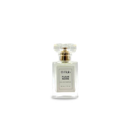 A rectangular clear perfume bottle with a clear faceted cap and a gold collar, featuring a white label that reads 'FLEUR NOIRE EAU DE PARFUM'.