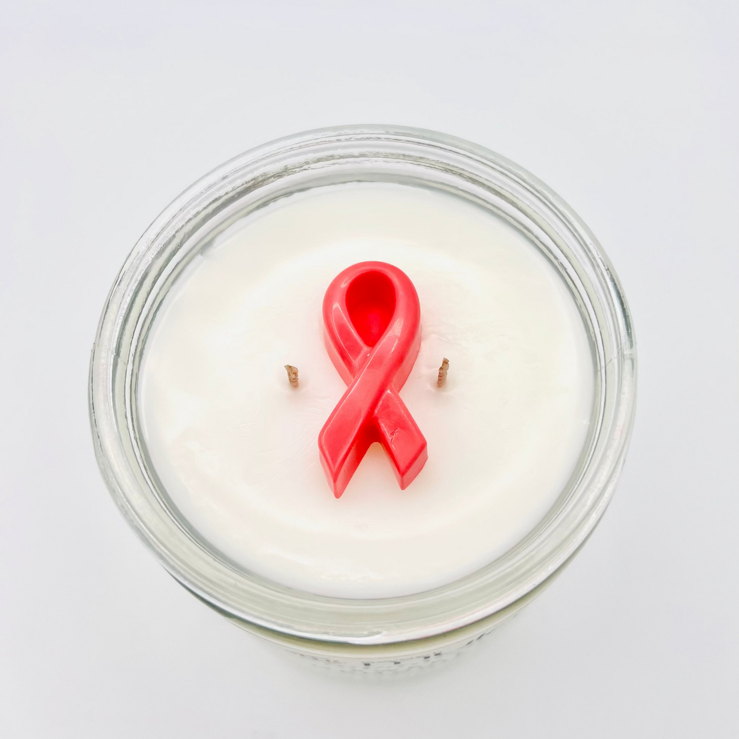 Candle in a glass jar with a pink cancer  ribbon on a white background