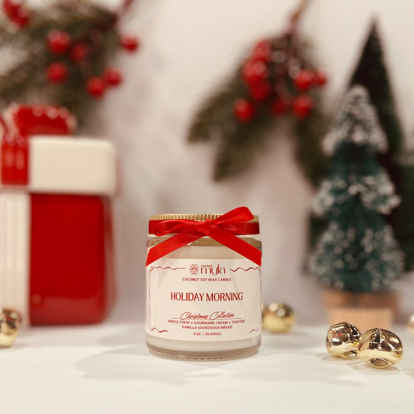 Candle jar with a red ribbon labeled Holiday Morning in front of Christmas decorations