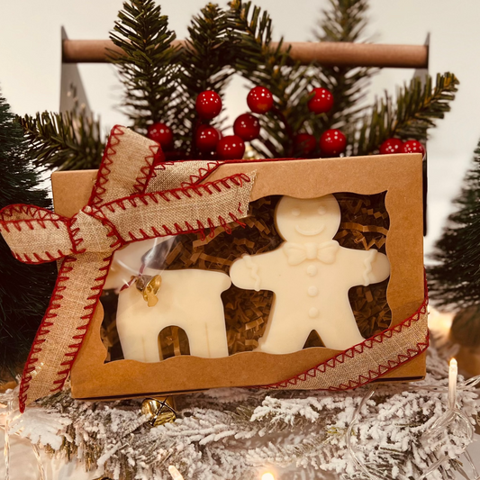 Decorative gingerbread man and reindeer wax melt/candle set in a box with Christmas trees in the background.