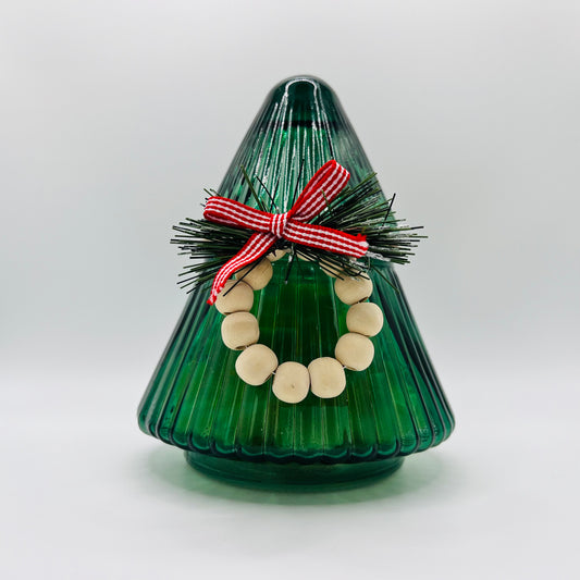 A glass jar shaped as a Christmas Tree with a wreath filled with wax melts.