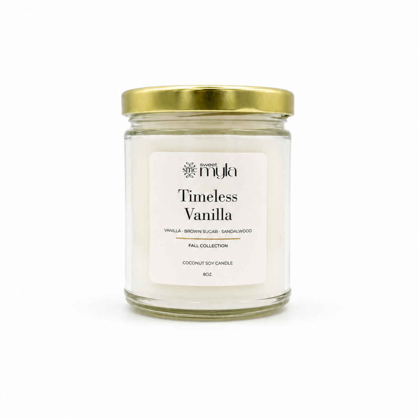 A 16 oz coconut soy candle in a clear glass jar with a white label reading 'Timeless Vanilla' by the brand 'Sweet Myla', topped with a metallic gold screw-on lid, set against a plain white background.