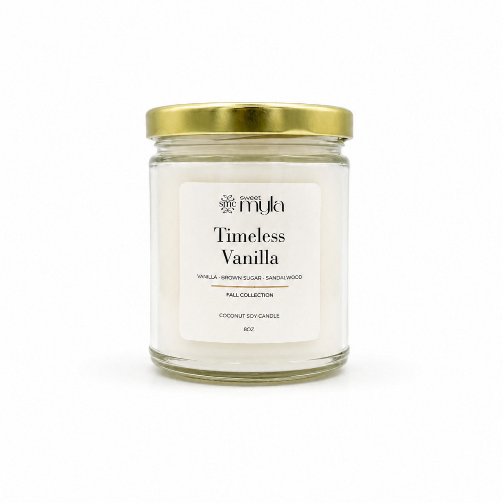 A 16 oz coconut soy candle in a clear glass jar with a white label reading 'Timeless Vanilla' by the brand 'Sweet Myla', topped with a metallic gold screw-on lid, set against a plain white background.
