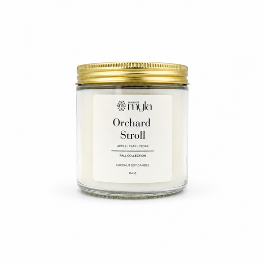 A 16 oz soy candle in a clear glass jar with a white label and a gold metal lid, labeled 'Orchard Stroll' by the brand Sweet Myla