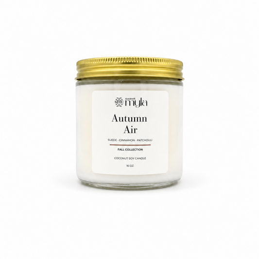A 16 oz coconut soy candle in a clear glass jar with a white label reading 'Autumn Air' by the brand 'Sweet Myla', topped with a metallic gold screw-on lid, set against a plain white background.